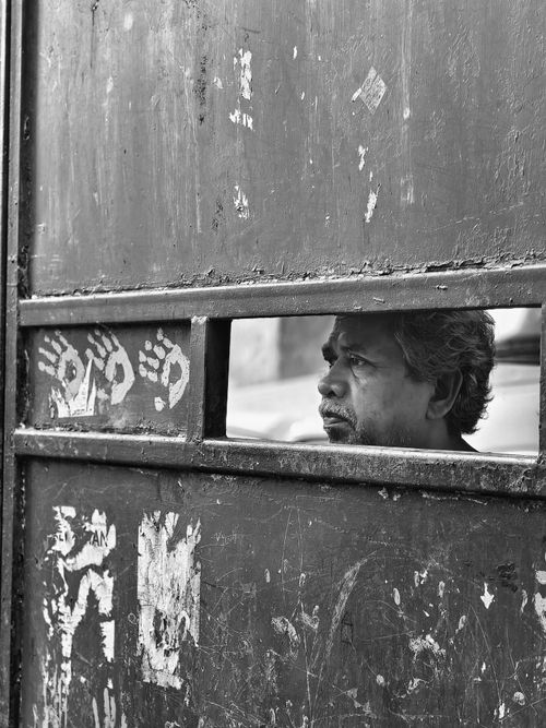 Free Black and white photo of a man looking through a gap in an aged door, Kolkata. Stock Photo