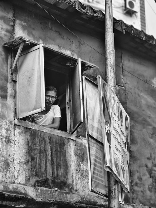 Free Black and white photo of a man peering out a window in Kolkata, India, capturing urban life. Stock Photo