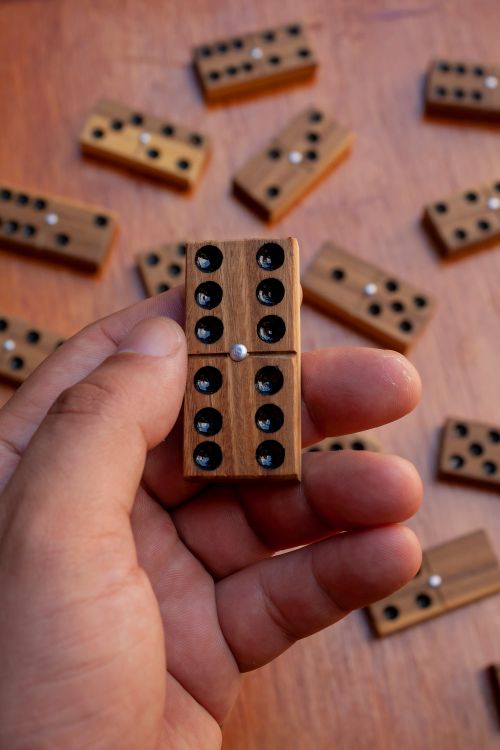 Free A hand holds a wooden domino tile on a table with scattered tiles. Stock Photo