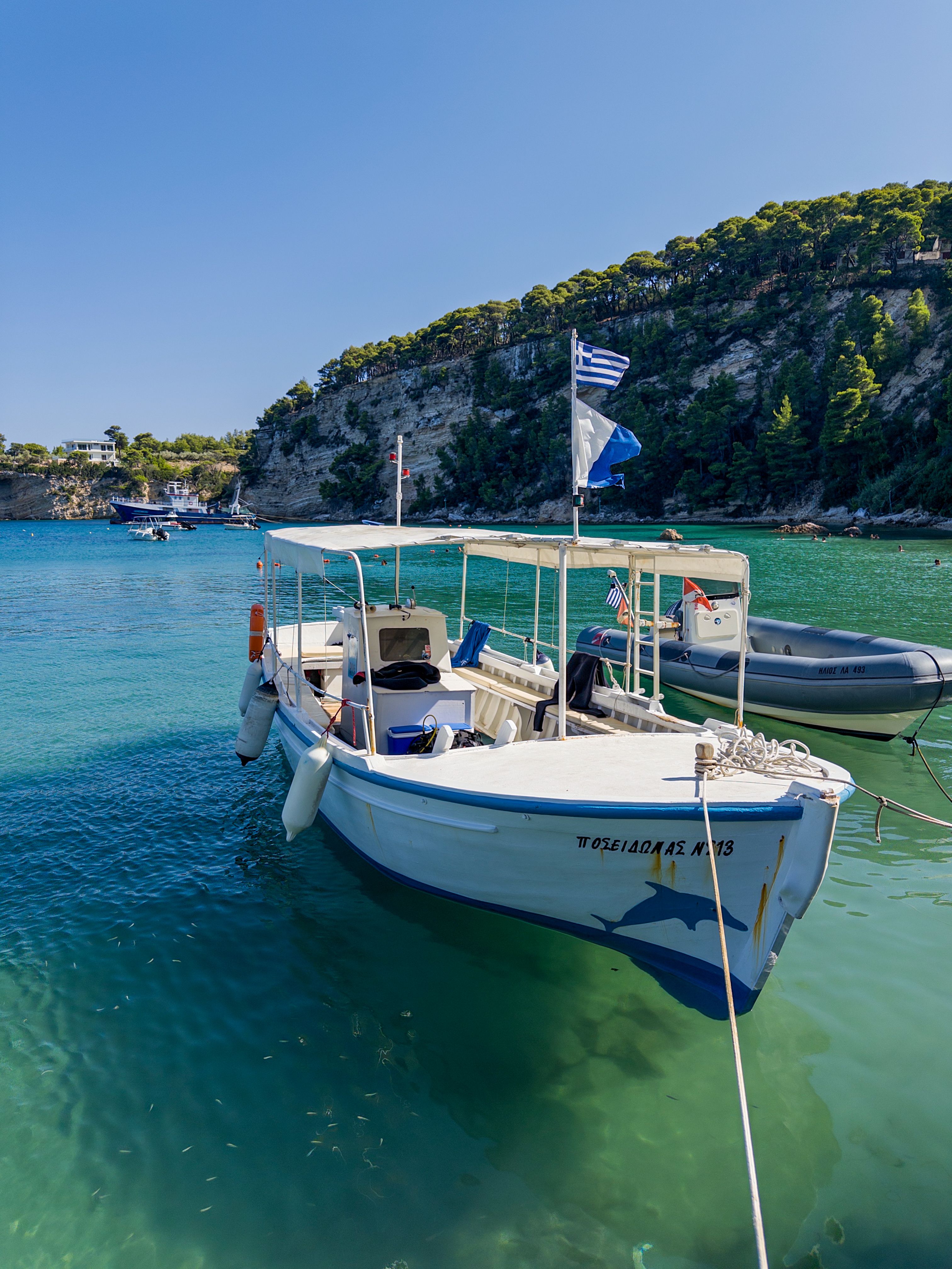 Traditional Greek boat on turquoise waters near a lush island coastline, under a sunny sky.
