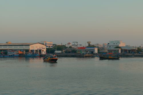 Free Coastal harbor view at dawn featuring colorful fishing boats and industrial buildings. Stock Photo