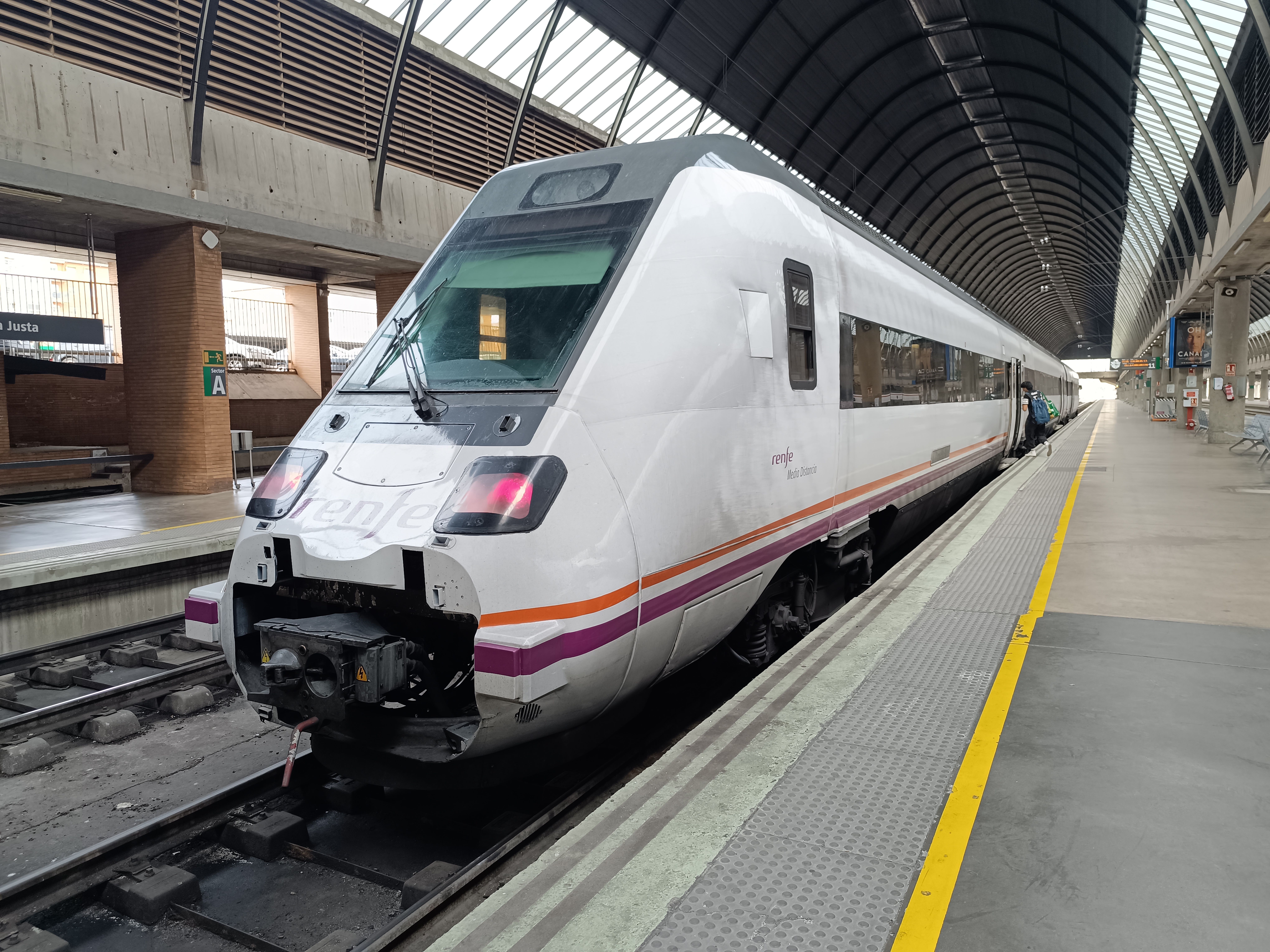 A white Renfe train standing at a platform under a vaulted roof of brick arches and glass