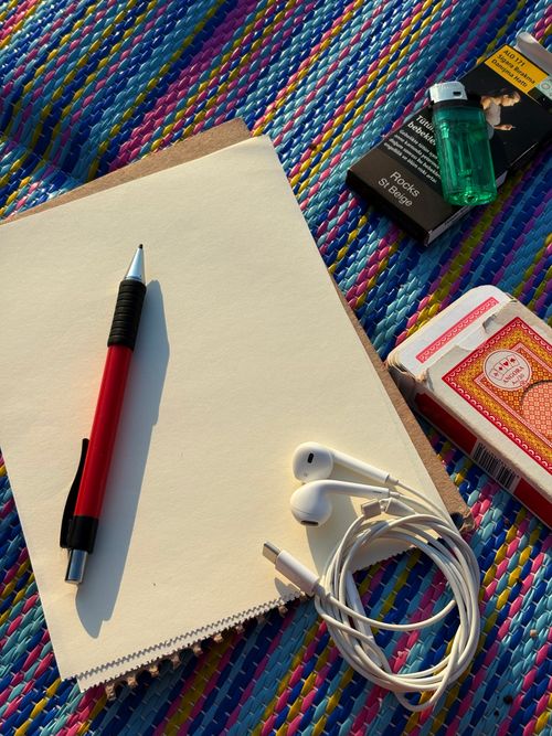 Free A colorful outdoor setting featuring a notebook, pen, earbuds, playing cards, and a lighter on a vibrant mat. Stock Photo