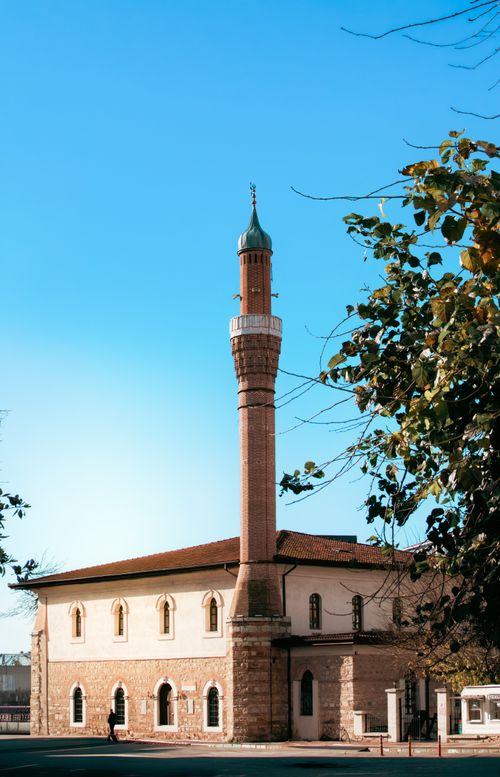 Free Charming historic mosque with a tall minaret surrounded by trees against a clear blue sky. Stock Photo