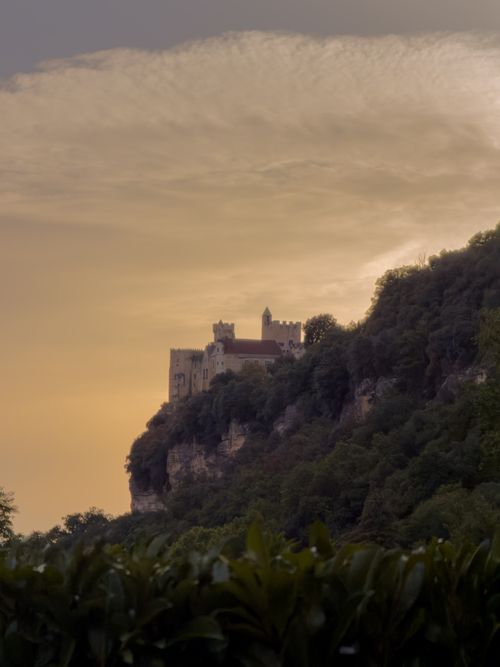 Free A stunning view of a medieval castle perched on a hill during sunset, surrounded by lush greenery. Stock Photo