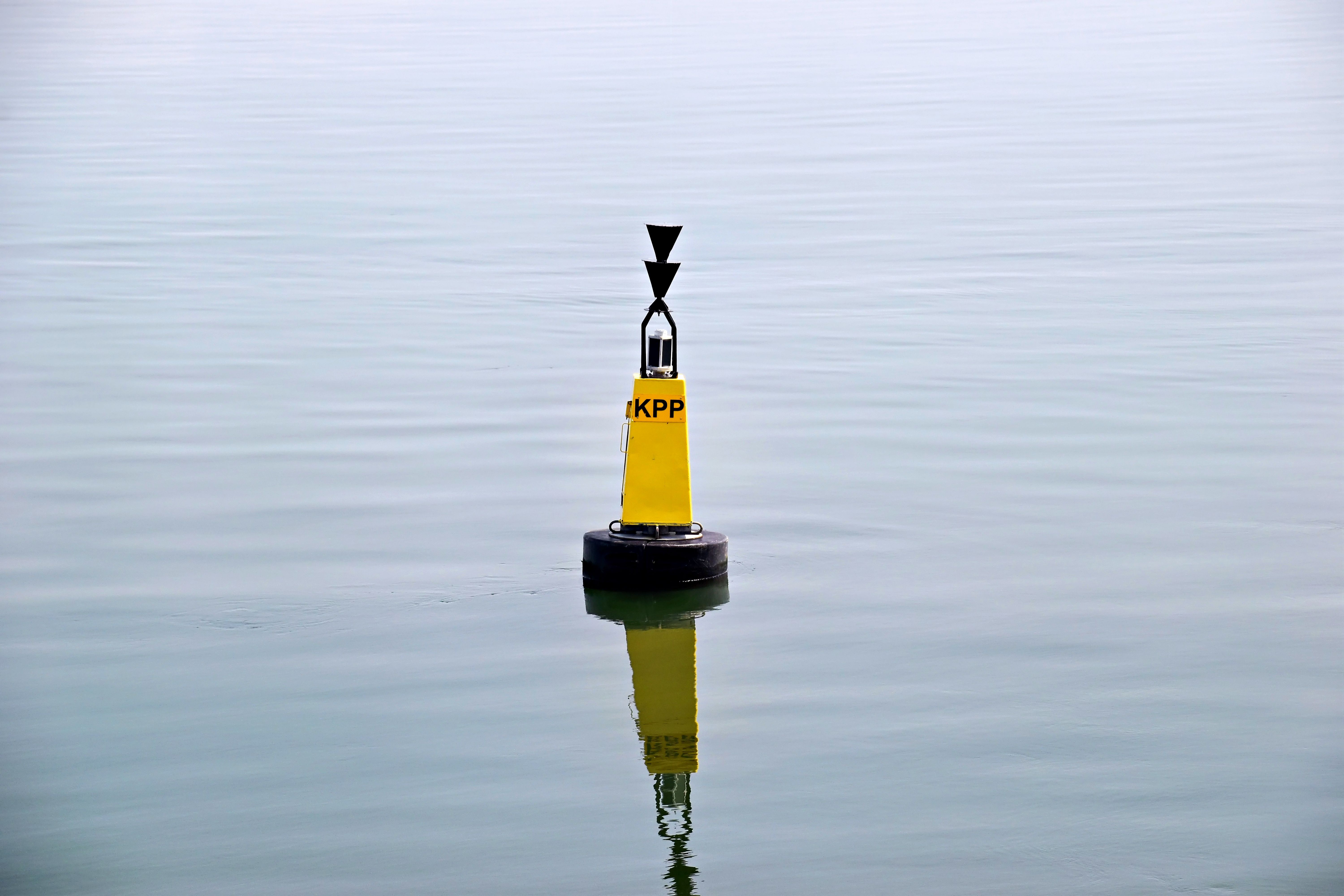 Yellow buoy labeled 'KPP' floats on smooth waters, reflecting the serene environment.
