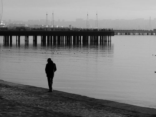 Free Black and white photo of a silhouette walking near a pier on a misty day. Stock Photo