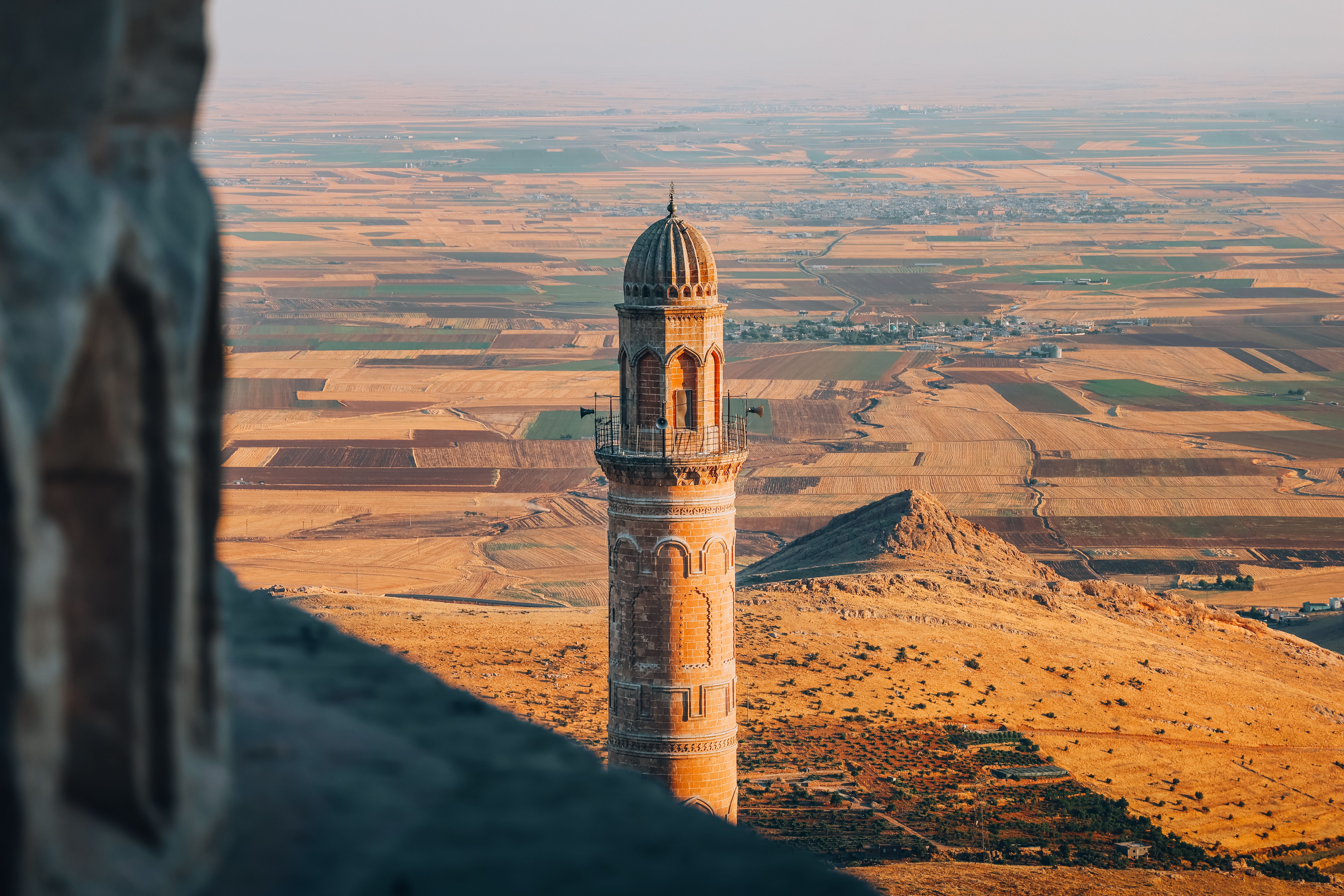 Captivating aerial shot of a historic minaret in Mardin, Türkiye, set against a vast golden landscape at sunset.
