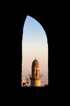 View of Mardin's mosque minaret through an archway, capturing a serene sunset.
