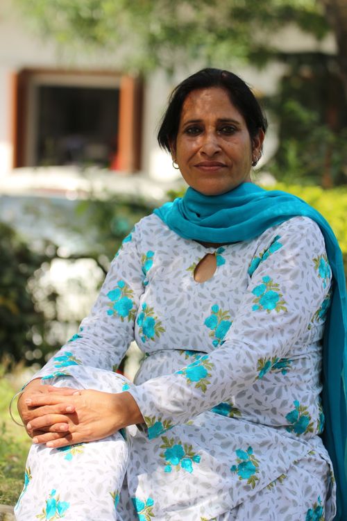 Free A woman sits outdoors in a garden, wearing a traditional floral outfit and scarf. Stock Photo