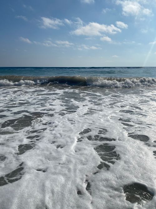 Free Serene beach scene with waves gently crashing on the shore under a clear blue sky in Peloponnese, Greece. Stock Photo