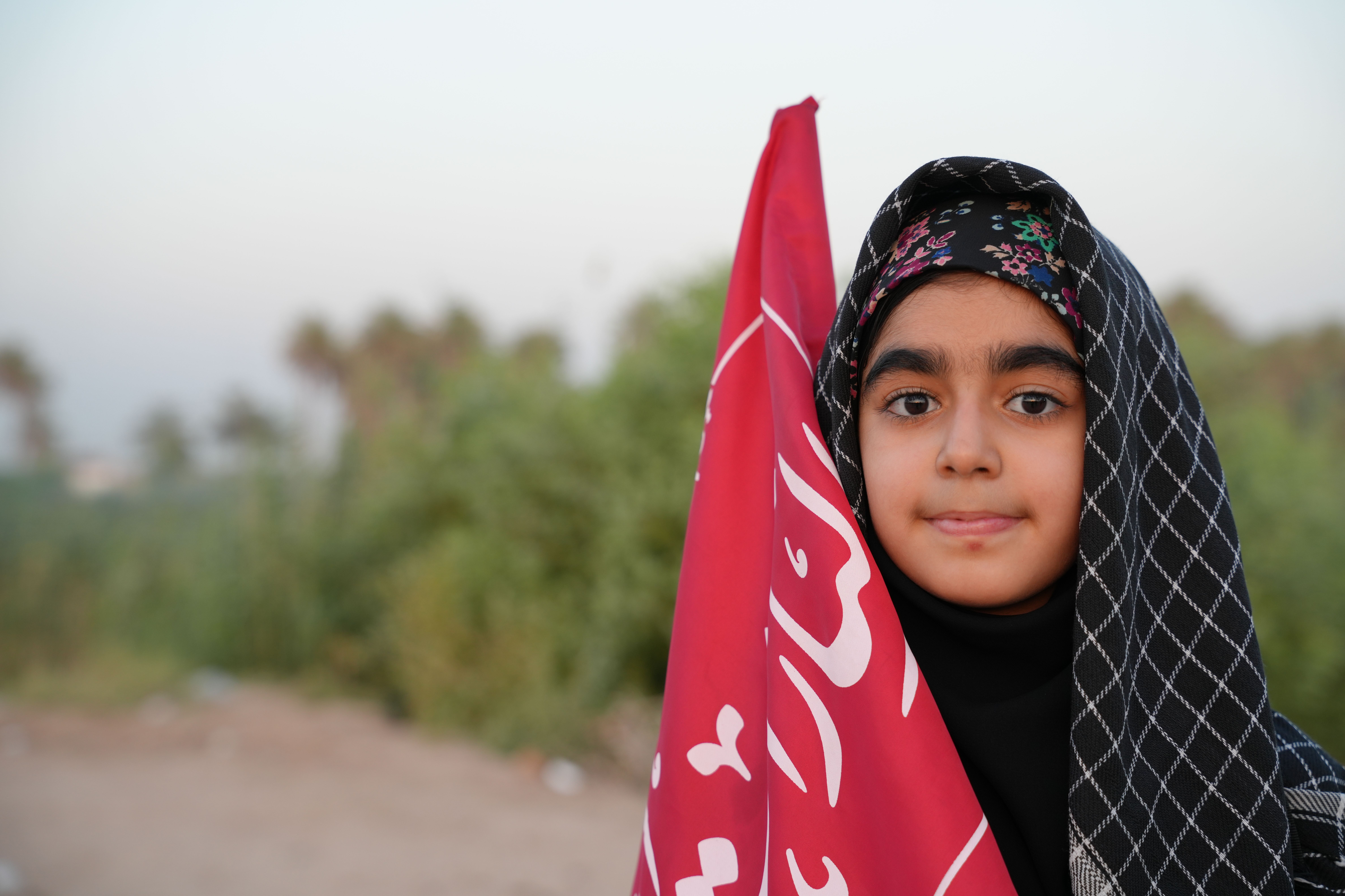 A young girl participates in the Arbaeen walk, holding a vibrant red flag in Karbala, Iraq.