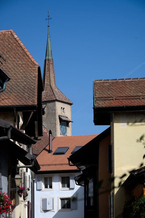 Free Picturesque street in a Swiss village with a prominent clock tower under clear skies. Stock Photo