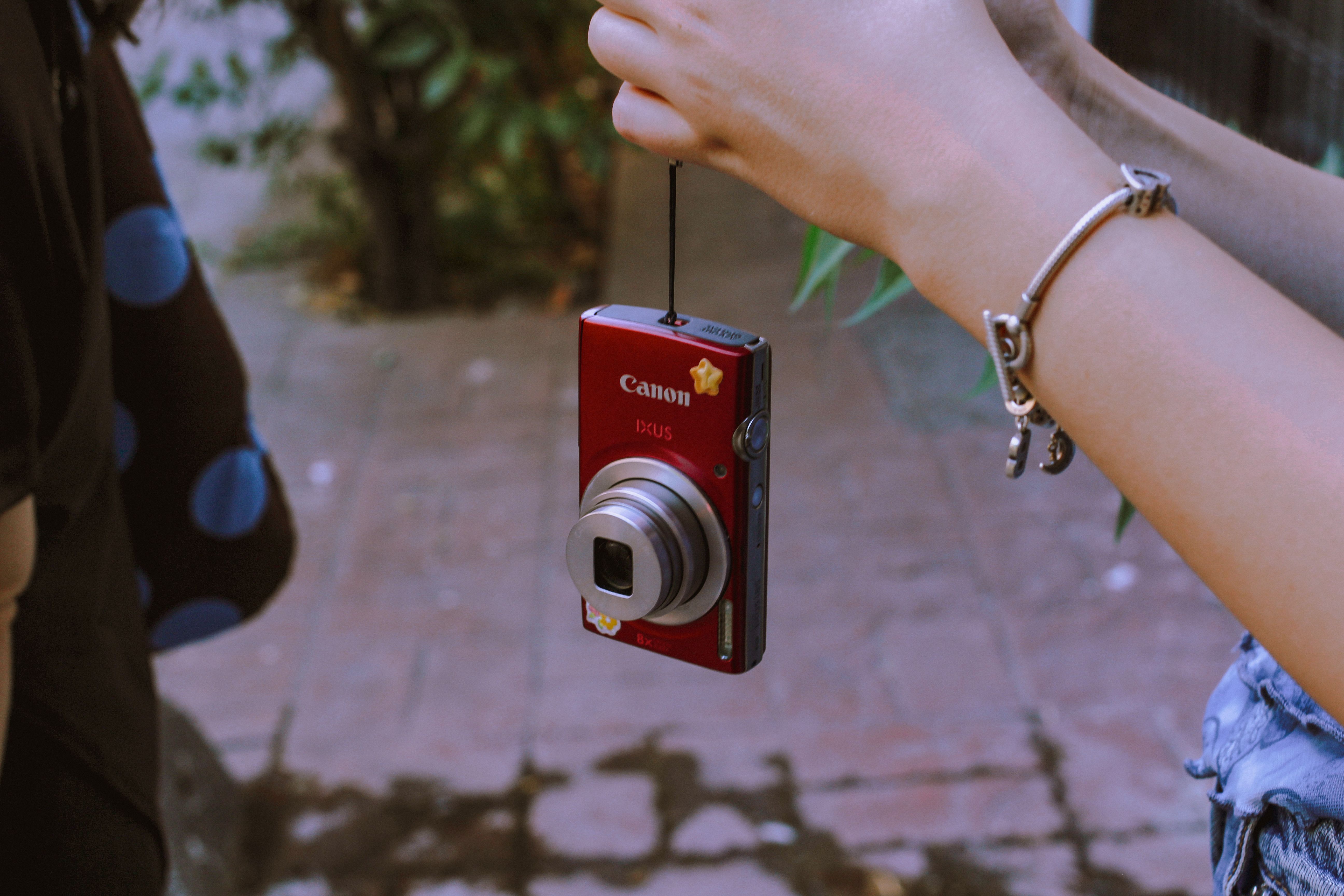 A close-up of a red digital camera hanging from a strap, outdoors.