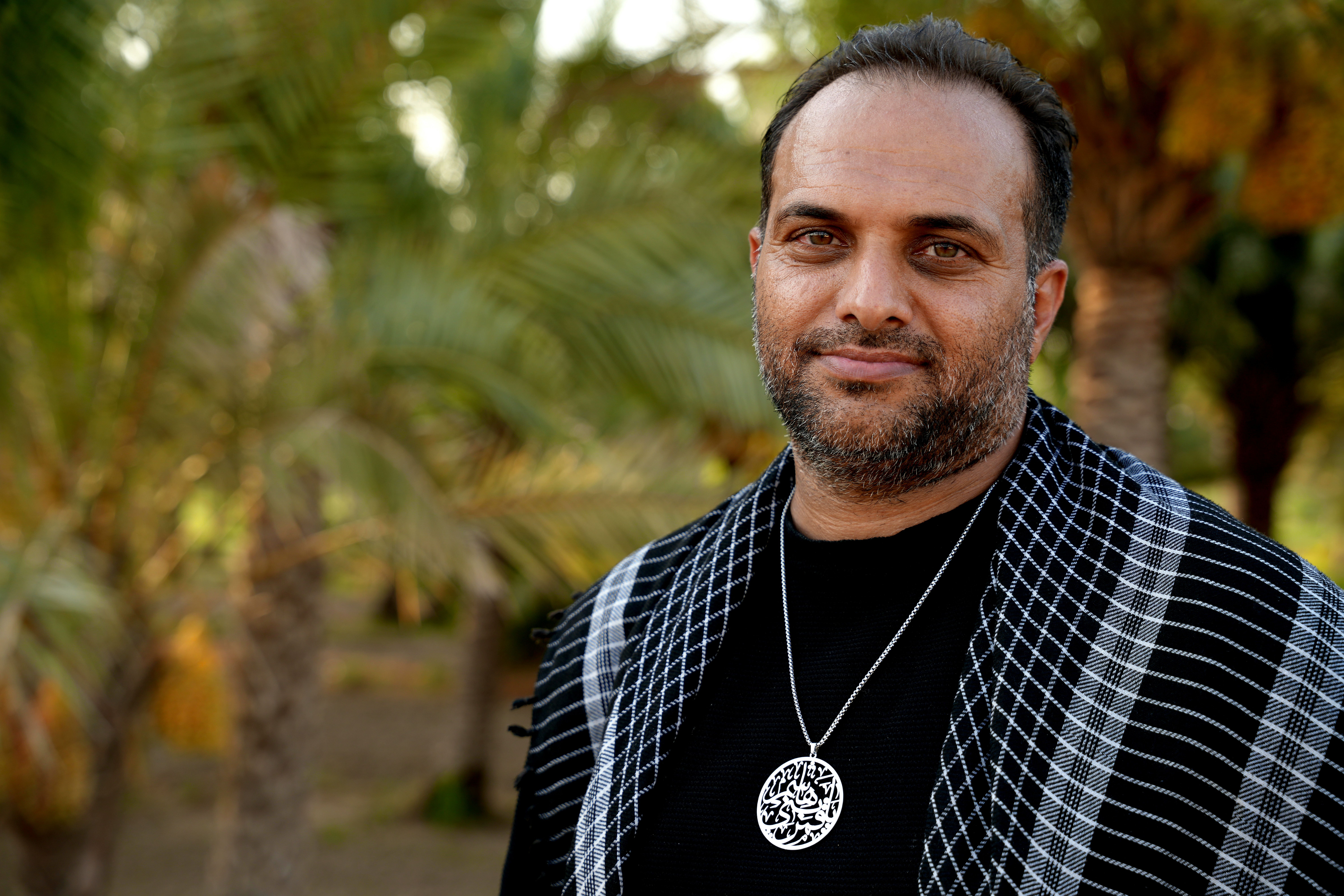 A serene portrait of a man wearing traditional attire in a palm grove in Karbala, Iraq.