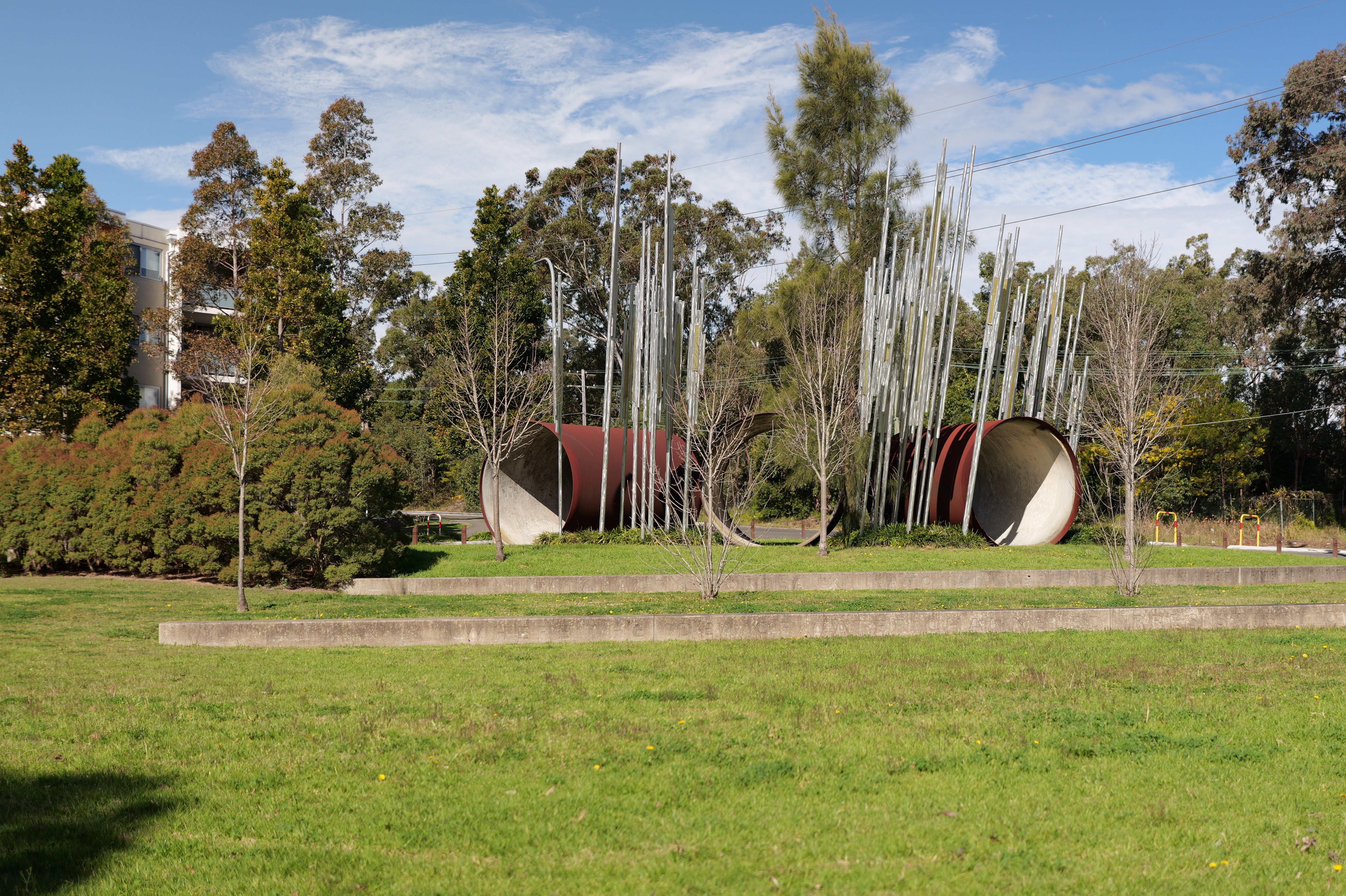 Contemporary art installation with steel tubes in a lush Sydney park on a sunny day.