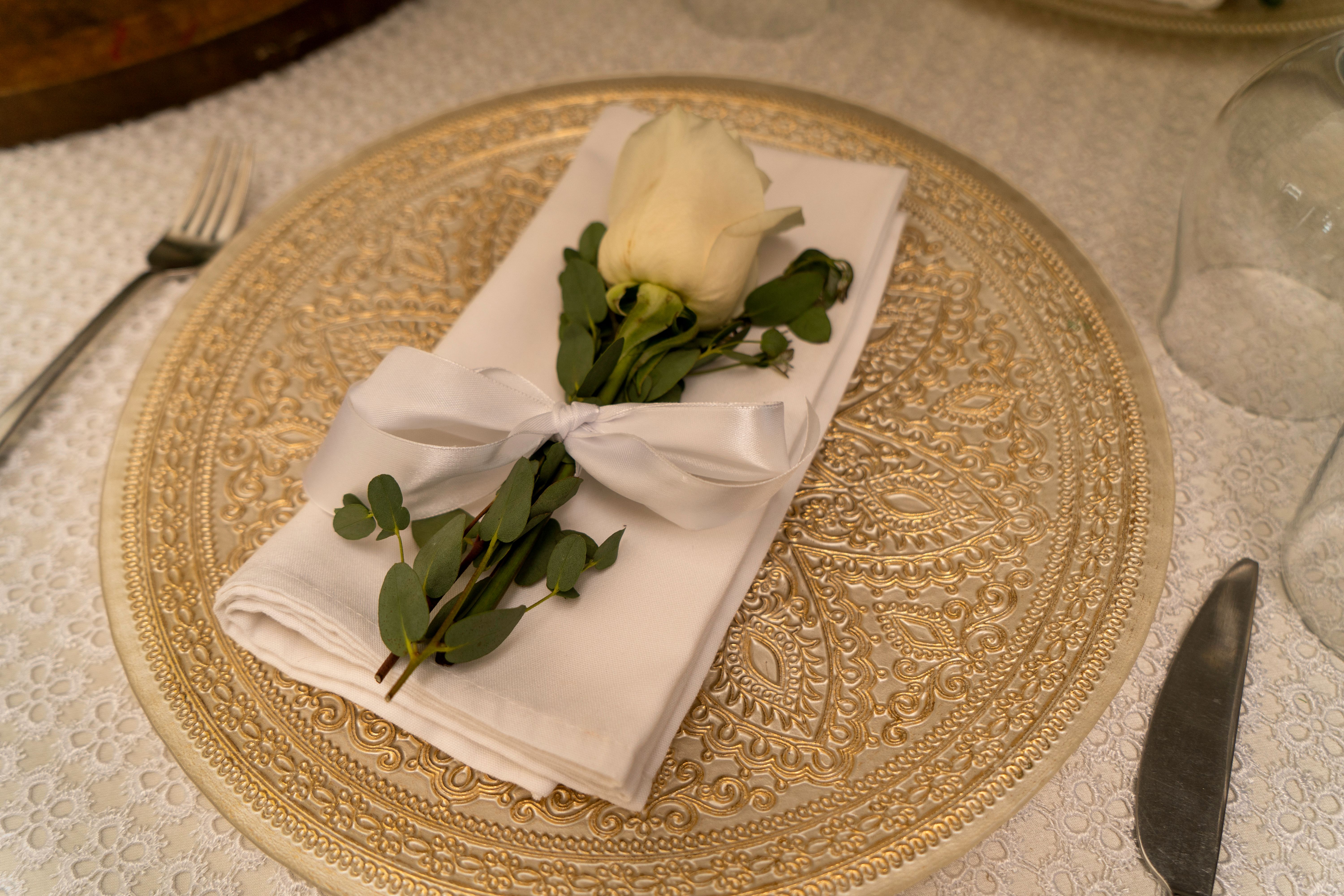 A luxurious table setting with an elegant white rose and gold charger plate, ideal for weddings or events.