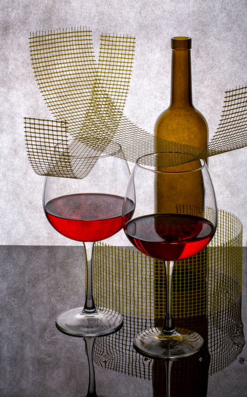 Free Elegant composition of red wine in glasses with artistic bottle and grid backdrop. Stock Photo