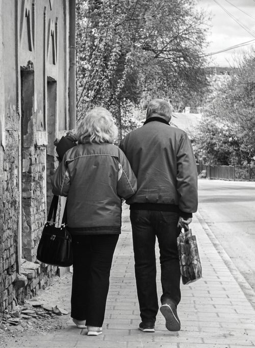 Free A senior couple walking arm in arm on a quiet city street, showcasing companionship and nostalgia. Stock Photo