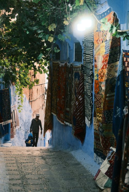 Free Colorful handwoven carpets hanging in a narrow alley of Chefchaouen, showcasing Moroccan culture and artistry. Stock Photo