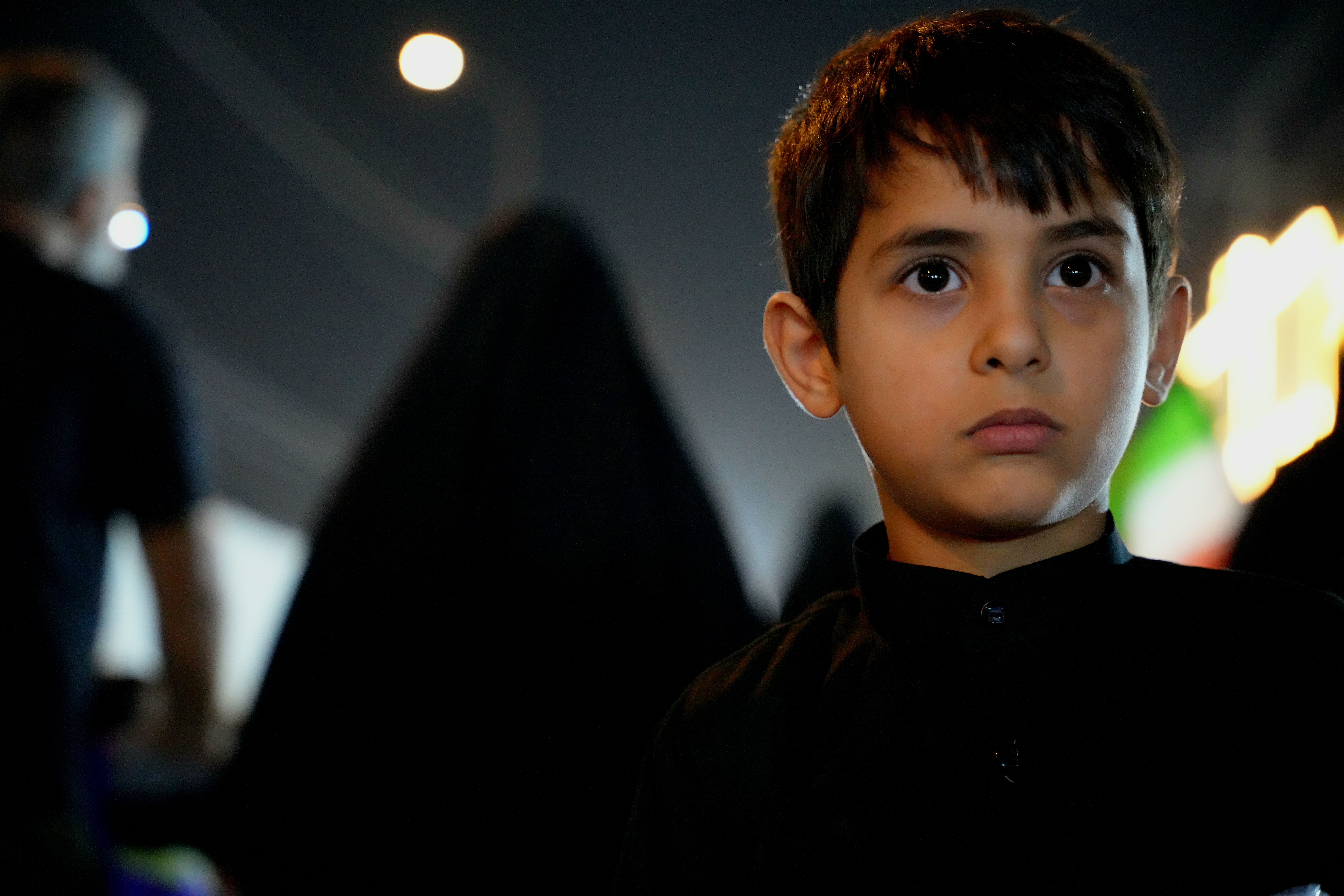 A young boy participates in the Arbaeen pilgrimage in Karbala, Iraq, against a night backdrop.
