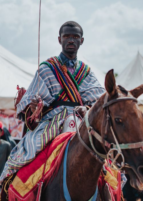 Free A rider in vibrant traditional attire participates in a cultural horse riding festival under a sunny sky. Stock Photo