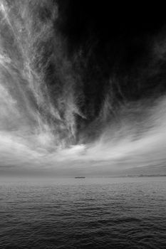 A striking black and white ocean scene with dramatic clouds and a distant ship on the horizon.