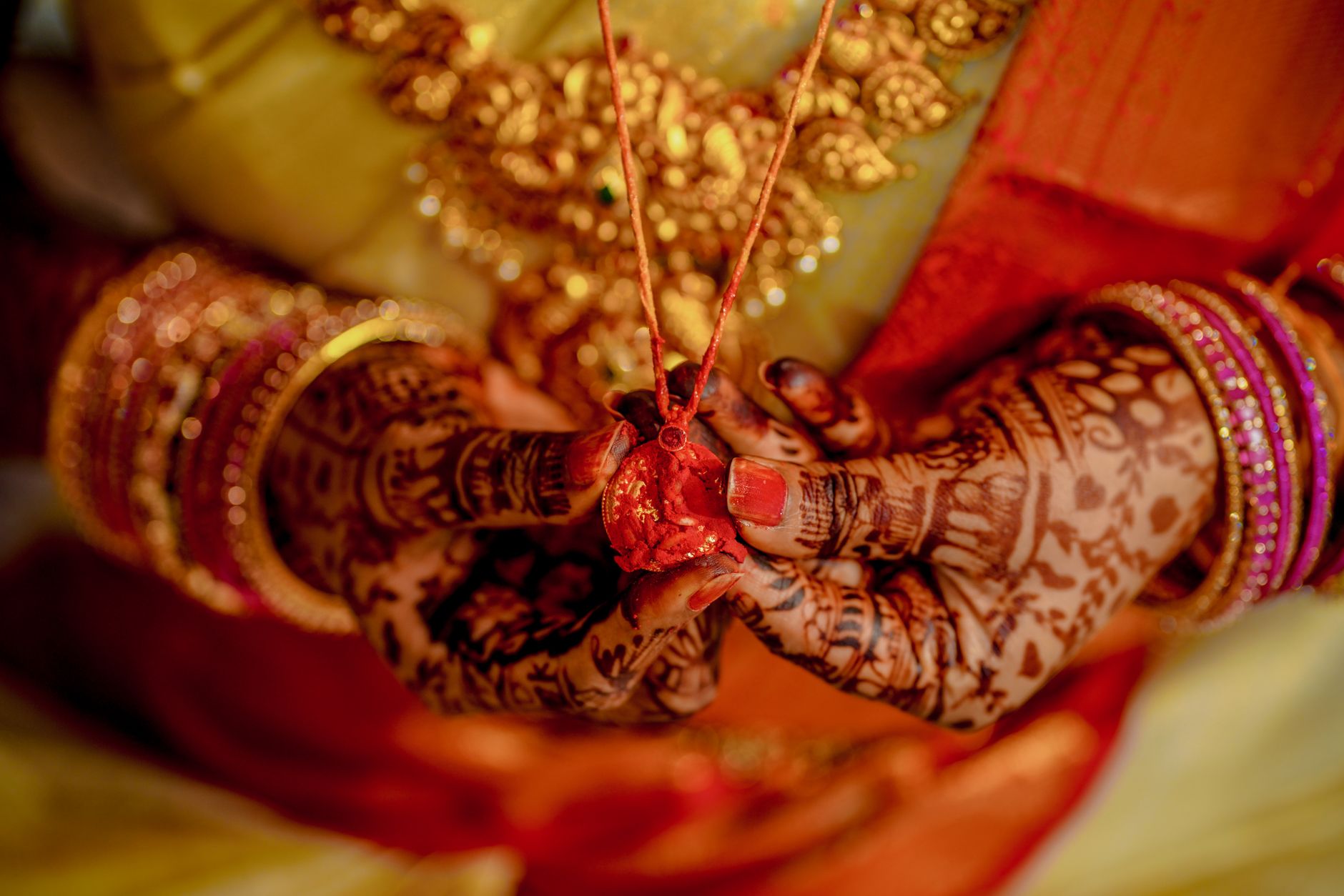 Standar Pelayanan Profesional dalam Menyediakan Paket Wedding Impian Anda 2 Close-up of Indian bride's hands with henna and gold jewelry, holding a mangalsutra.