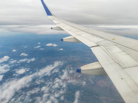 Airplane wing view with clouds and landscapes from high altitude.