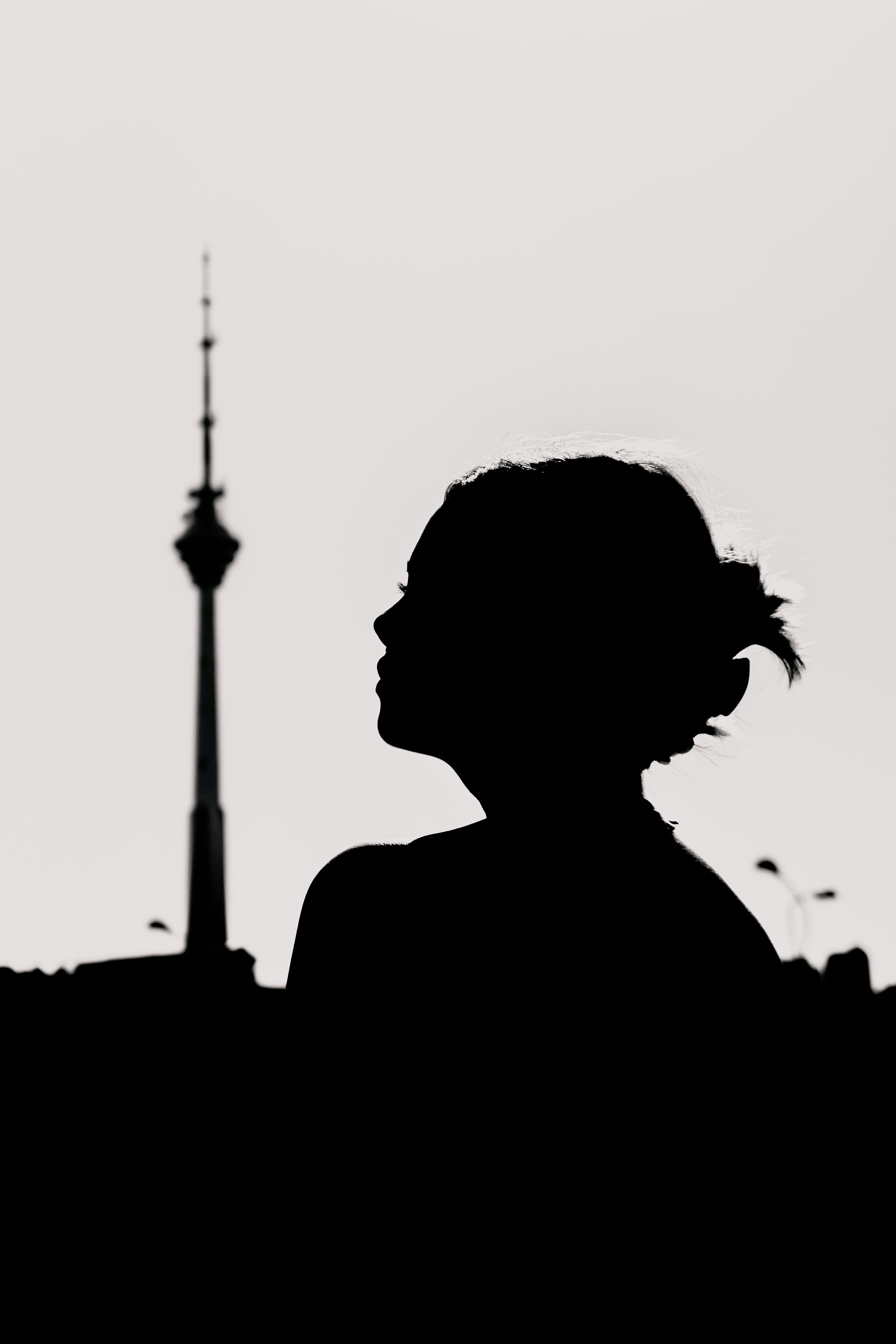 Silhouette of a woman against the skyline with a TV tower in the background during sunset, creating a moody atmosphere.