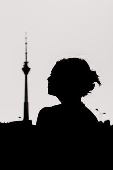 Silhouette of a woman against the skyline with a TV tower in the background during sunset, creating a moody atmosphere.