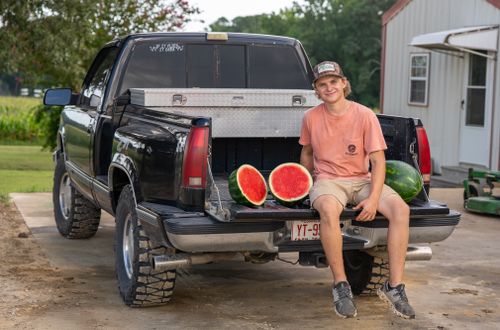 Free Young man sitting on a pickup truck with watermelons, a sunny day in the countryside. Stock Photo