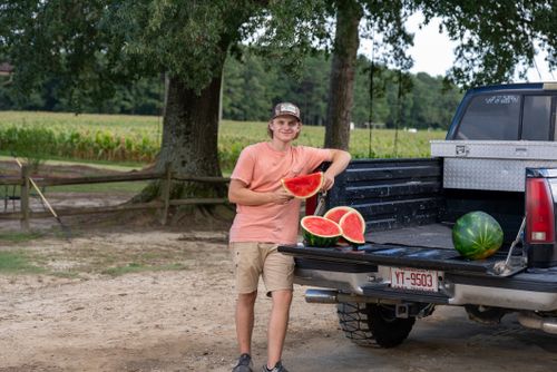 Free Smiling young farmer holding ripe watermelon slices by a pickup truck in a rural setting. Stock Photo
