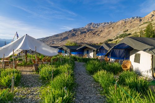 Free Beautiful mountain campsite with tents, wicker chairs, and lush greenery under a clear blue sky. Stock Photo
