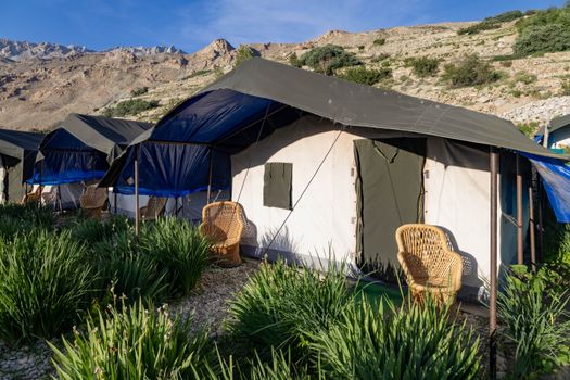 Serene outdoor campsite with tents and wicker chairs against a beautiful mountain backdrop.
