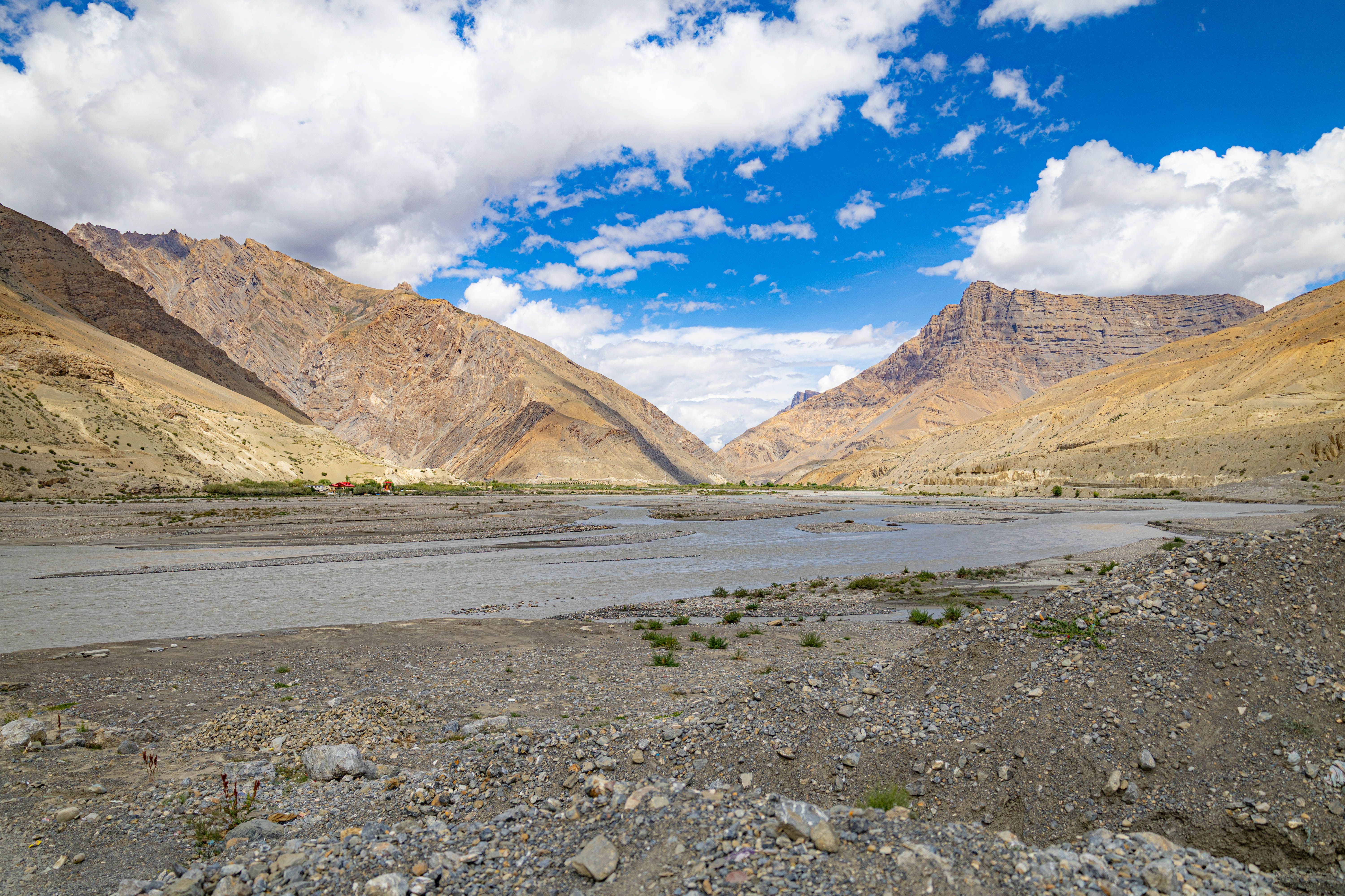 Wide view of a mountain valley with a river under a vibrant blue sky and fluffy clouds.