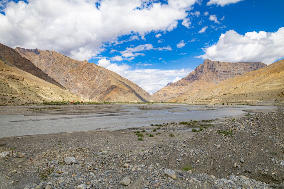 Wide view of a mountain valley with a river under a vibrant blue sky and fluffy clouds.