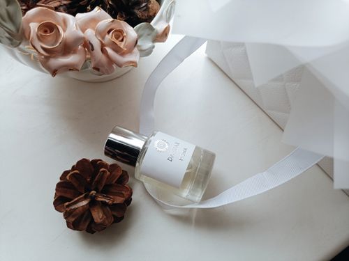 Free A stylish perfume bottle surrounded by decorative roses and a pinecone on a light surface. Stock Photo