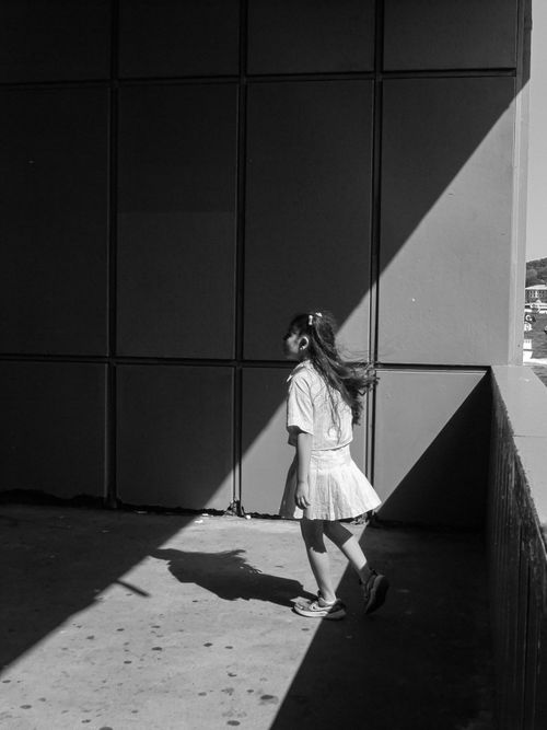 Free Black and white photo of a girl walking through contrasting light and shadow. Stock Photo