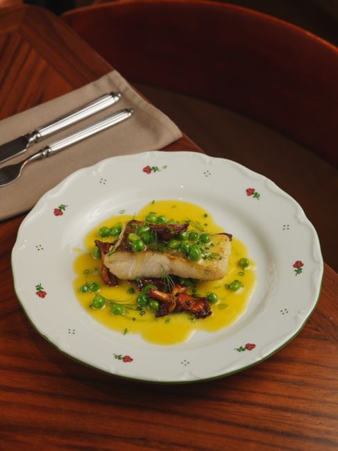 Two glossy, caramelized miso black cod fillets on a white plate, the surface deeply browned and glazed, with scallions scattered over the top.
