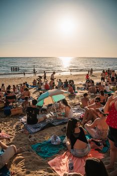 A lively crowd enjoys a beach party during sunset, with people socializing and relaxing by the sea.
