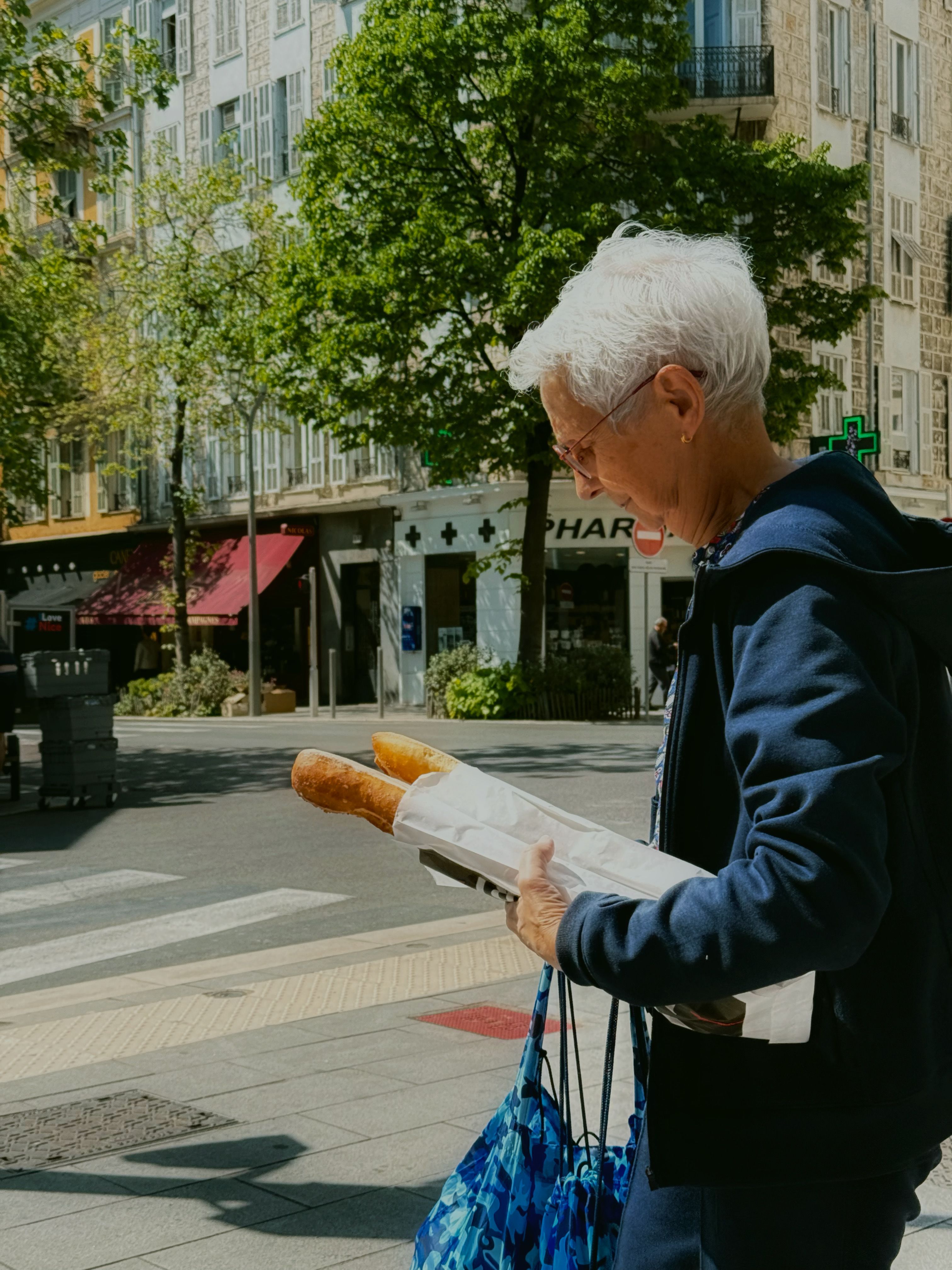 Senior woman carrying baguettes on a sunny day in Nice, France street scene.