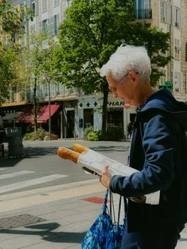 Senior woman carrying baguettes on a sunny day in Nice, France street scene.