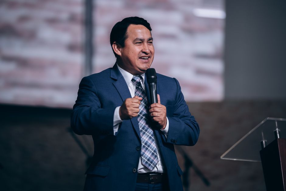 A confident speaker in a suit holding a microphone, engaging an audience indoors.