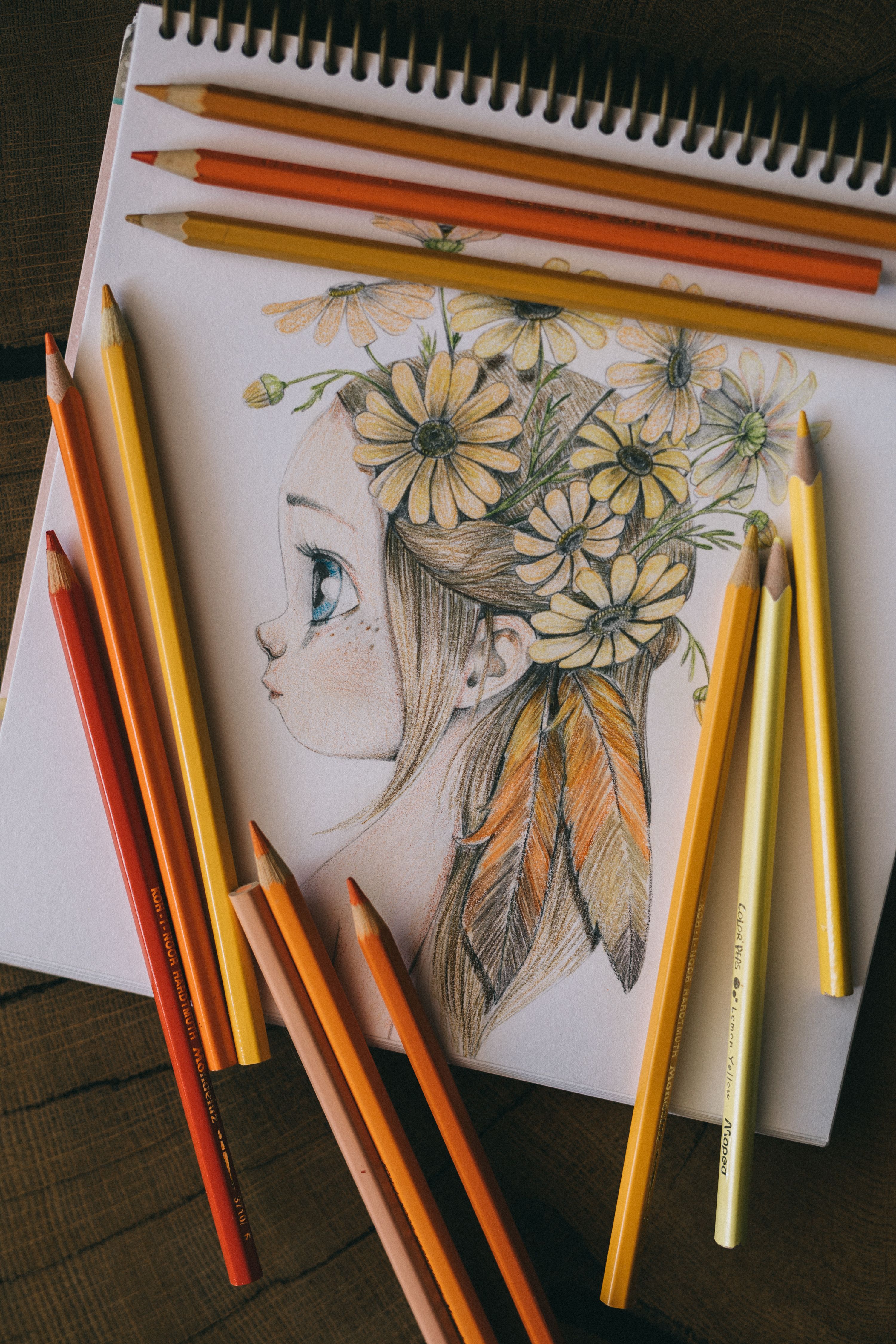 Color pencils surround a sketch of a girl with floral headpiece, showcasing artistic talent.