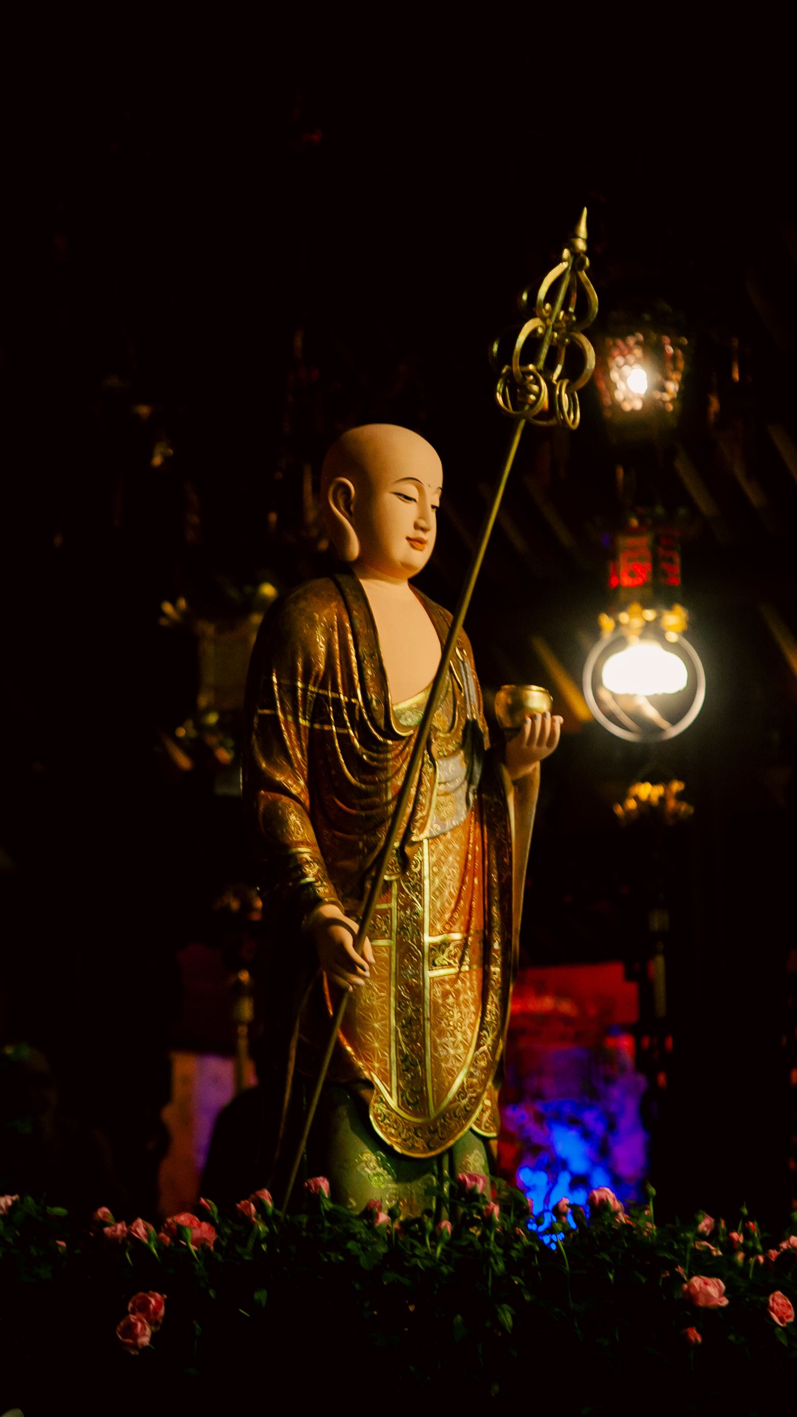 A serene Buddhist monk statue at a temple in Ho Chi Minh City, Vietnam, surrounded by flowers and warm lighting.