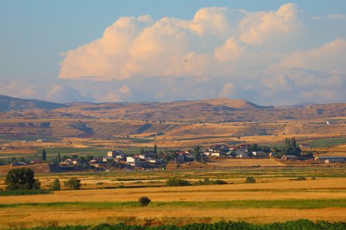Free Idyllic rural village with rolling hills and vast fields under a cloudy sky. Stock Photo