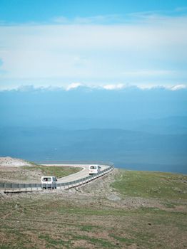 White vans travel a winding mountain road under clear blue skies.