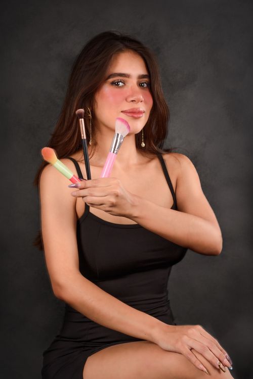 Free A young woman in a studio setting showcases an array of makeup brushes with a confident smile. Stock Photo