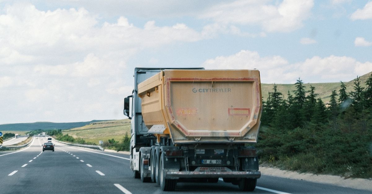 A cargo truck travels on a highway beneath a bright blue sky with fluffy clouds.